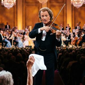 “HE STOPPED MID-MELODY… BECAUSE HE SAW A WHITE HANDKERCHIEF.” Under the warm golden lights, André Rieu suddenly slowed, his eyes drifting toward the front row.